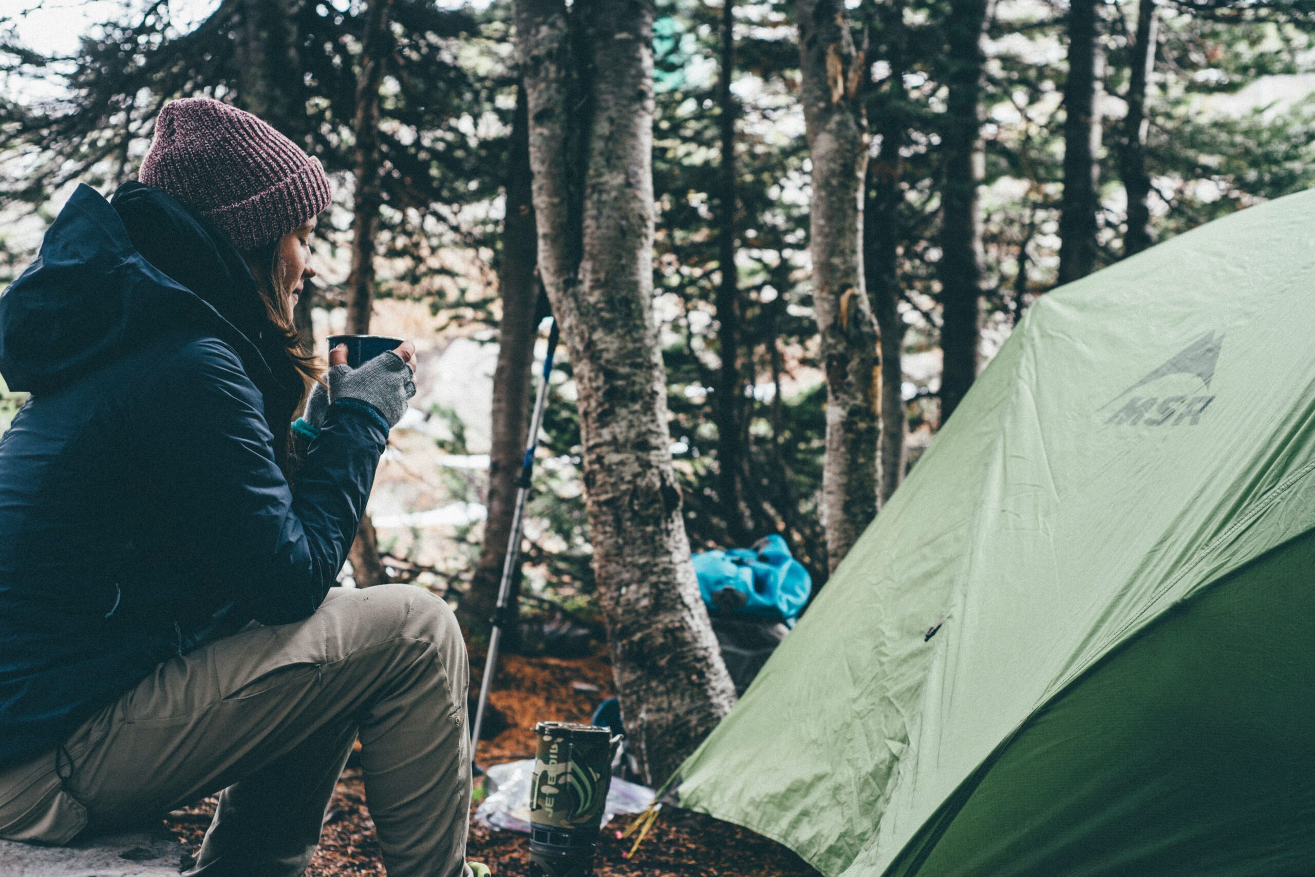 female drinking coffee by tent outside